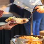 Staff serving assorted hot food along a cafeteria buffet line