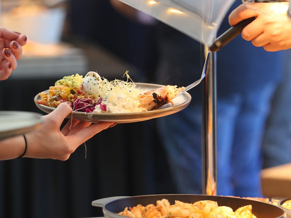 Staff serving assorted hot food along a cafeteria buffet line